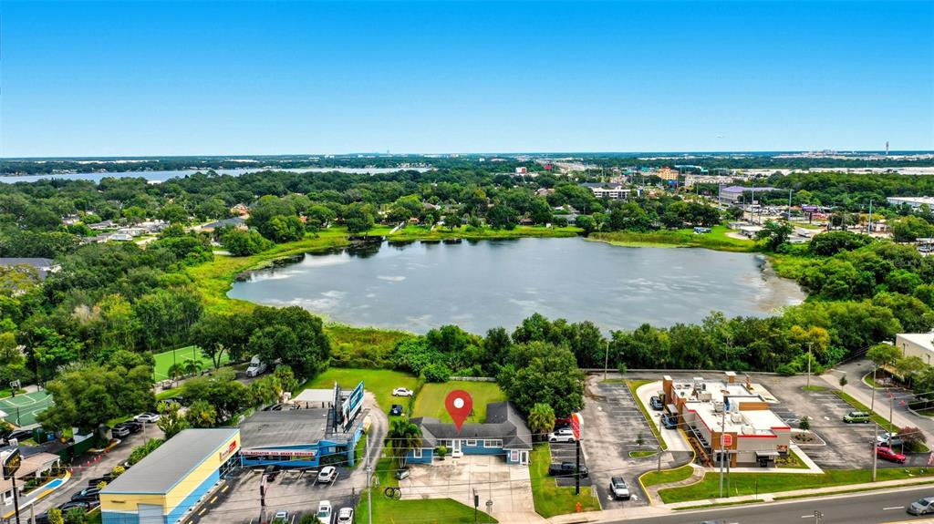An aerial view shows a commercial building with a red location pin near a lake — 8027 S ORANGE AVENUE, ORLANDO, FL