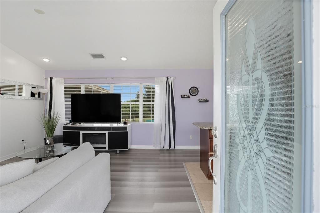 A living room with light purple walls, gray wood-look flooring, and a glass-paneled front door — 8027 S ORANGE AVENUE, ORLANDO, FL