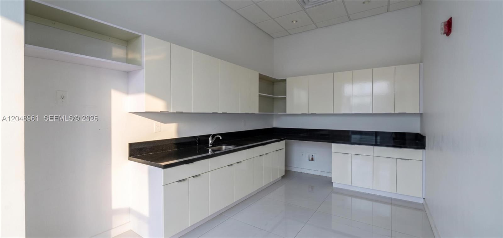 A kitchen features white cabinets, black countertops, and light-colored tile flooring — 1200 Brickell Ave # 200C, Miami FL 33131, MIAMI, FL