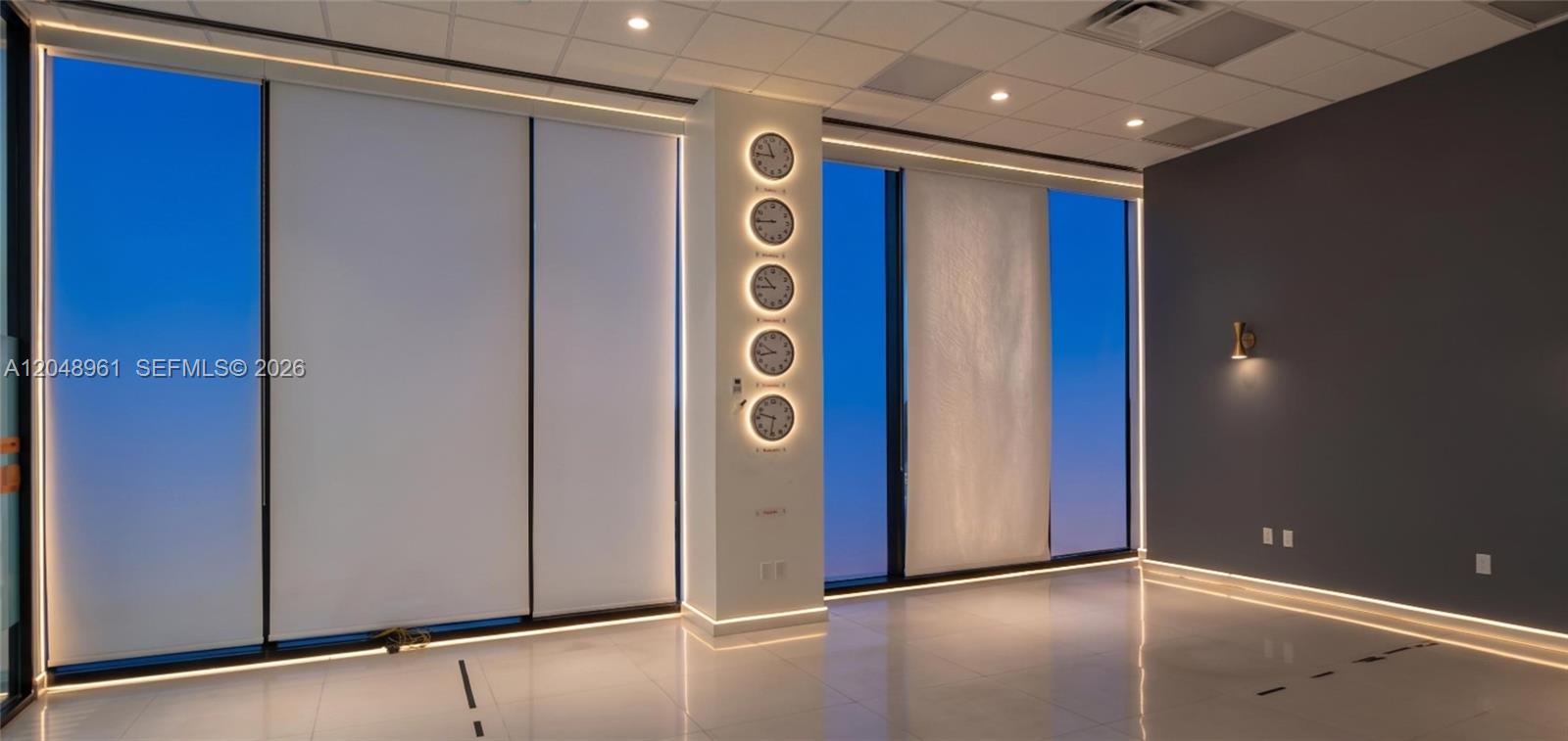 A modern office space features floor-to-ceiling windows, tiled floors, and a column displaying five clocks — 1200 Brickell Ave # 200C, Miami FL 33131, MIAMI, FL