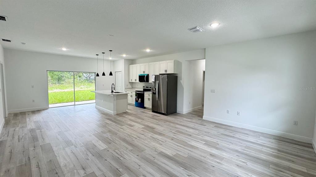 An open-concept kitchen and living area features light wood-look flooring, white cabinets, and stainless appliances — 2456 W MAGENTA DRIVE, CITRUS SPRINGS, FL