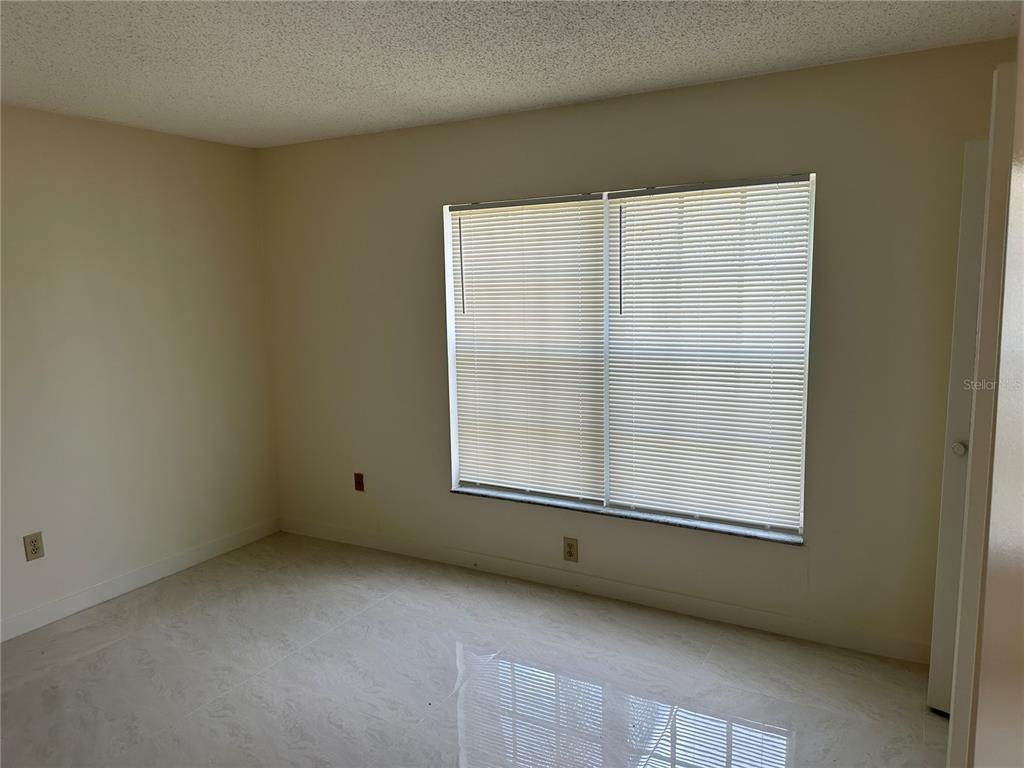 An empty bedroom features light-colored tile flooring, off-white walls, and a window with blinds — 5915 TAYWOOD DRIVE, TAMPA, FL