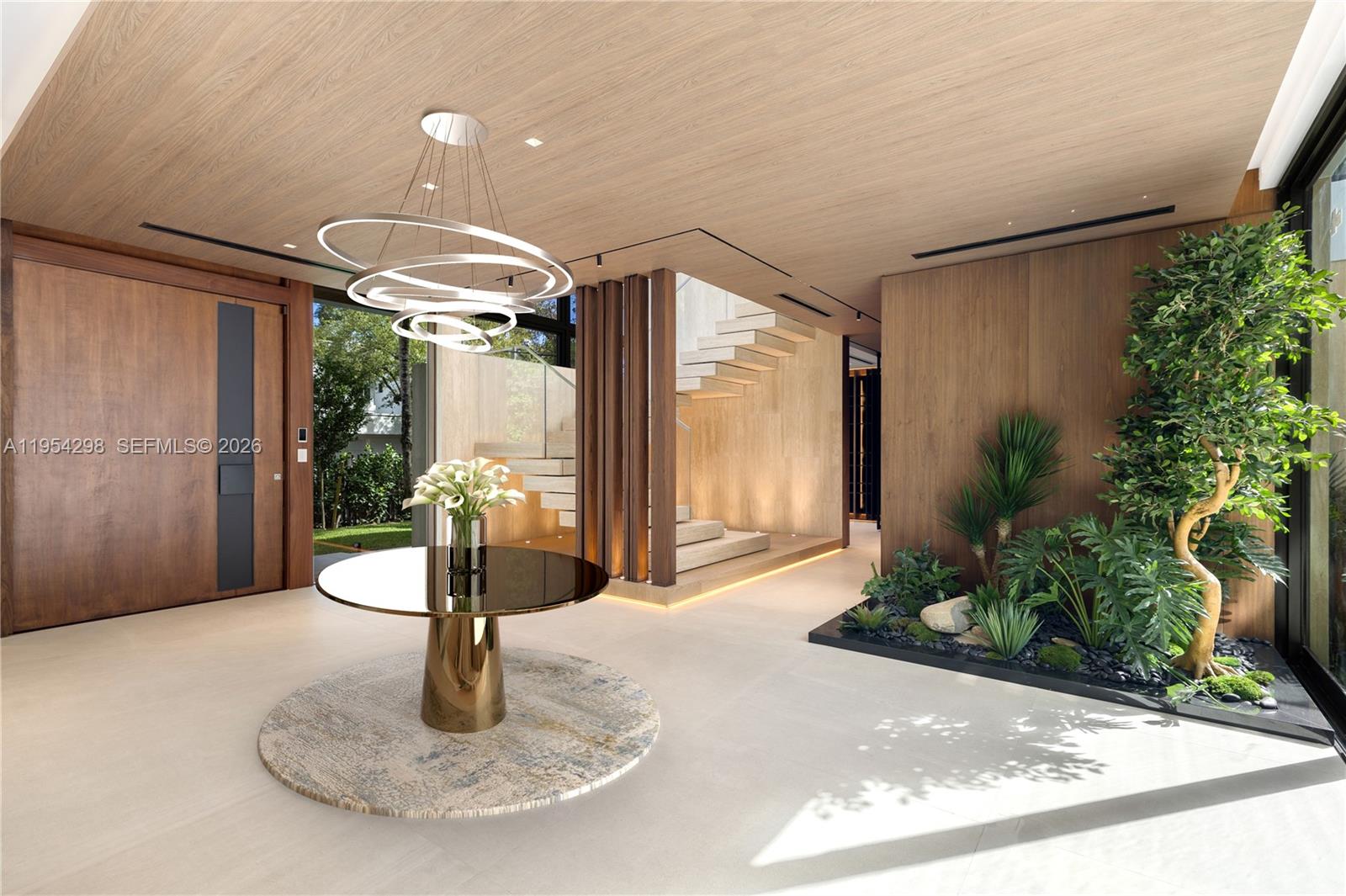 A modern entryway features a circular table, a sculptural chandelier, a staircase, and indoor plants — 3210 Coacoochee St, Miami FL 33133, MIAMI, FL
