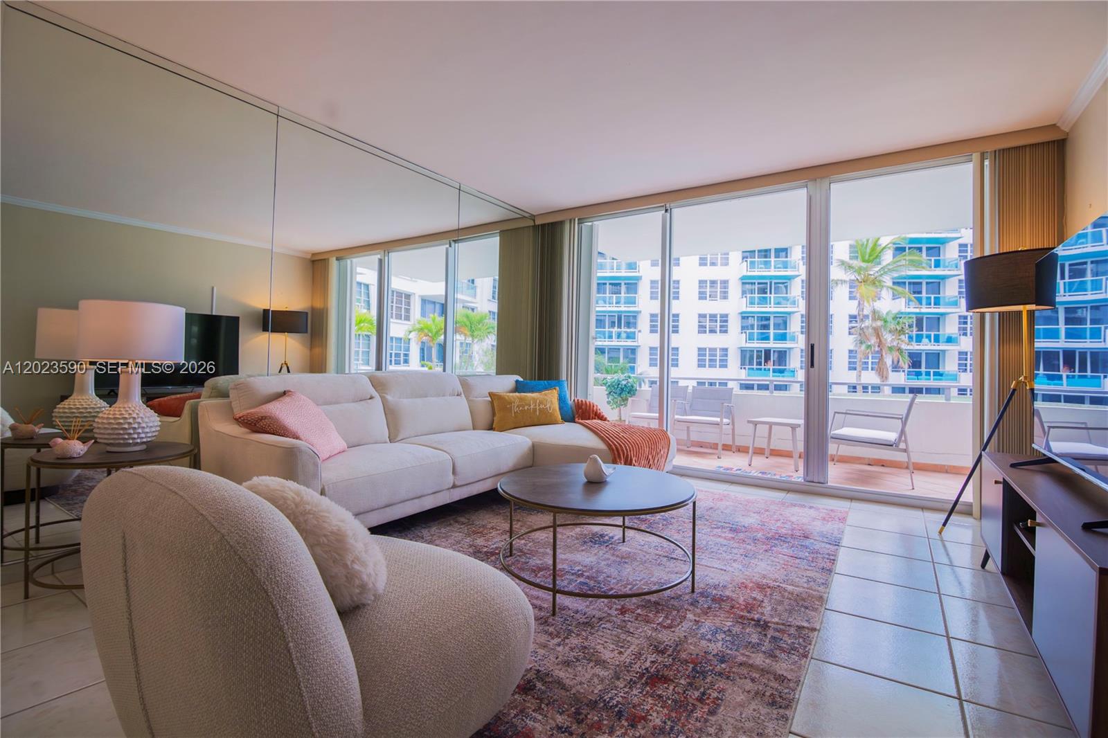 A living room features a sectional sofa, a round coffee table, and a mirrored wall — 5151 Collins Ave # 428, Miami Beach FL 33140, MIAMI BEACH, FL