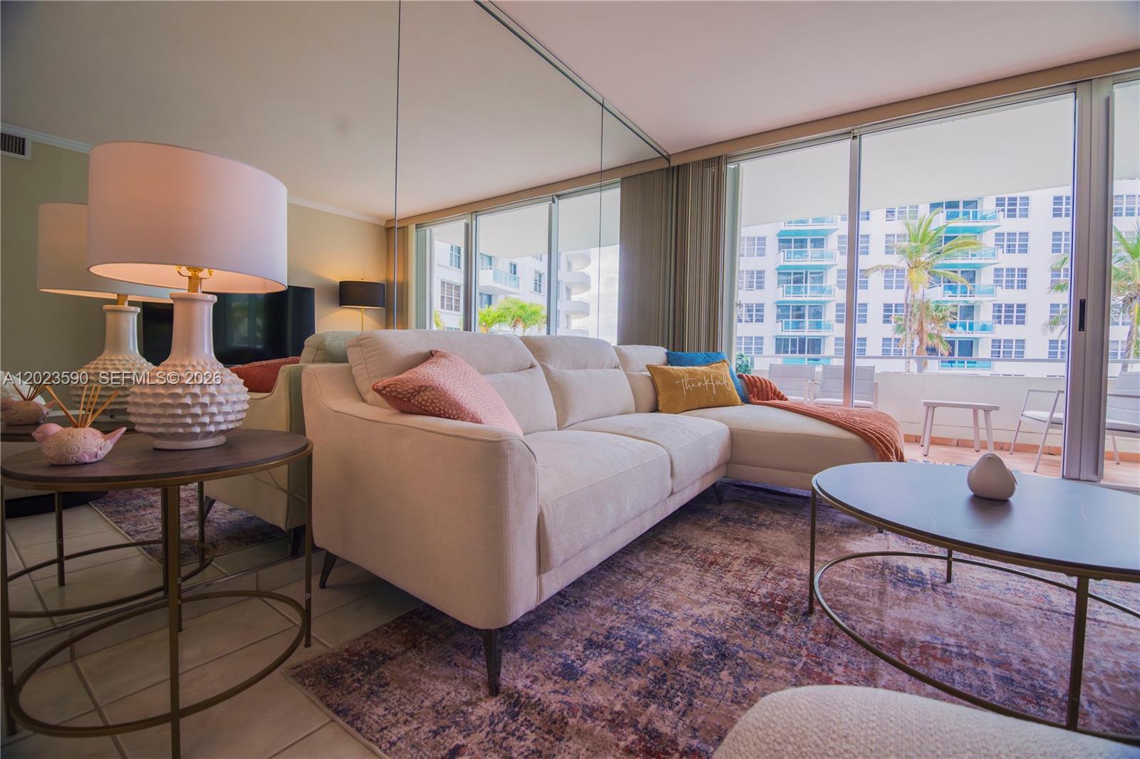 A living room features a beige sectional sofa, a round coffee table, and mirrored walls — 5151 Collins Ave # 428, Miami Beach FL 33140, MIAMI BEACH, FL