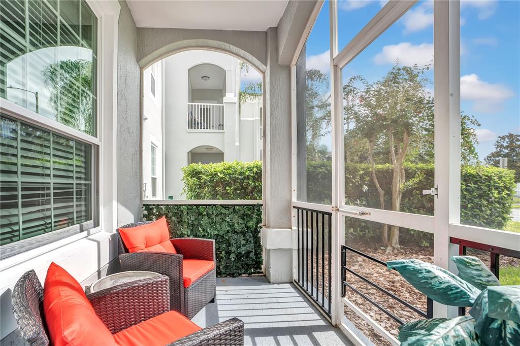 A screened-in balcony features two wicker chairs with orange cushions and a view of landscaping — 2307 BUTTERFLY PALM WAY UNIT 104, KISSIMMEE, FL