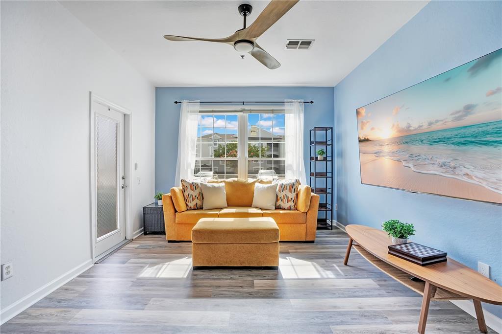 A living room features a yellow sofa, a matching ottoman, and a large wall-mounted television — 2307 BUTTERFLY PALM WAY UNIT 104, KISSIMMEE, FL