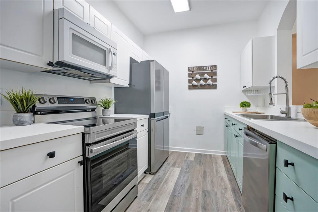 A galley kitchen features white upper cabinets, light green lower cabinets, and stainless steel appliances — 2307 BUTTERFLY PALM WAY UNIT 104, KISSIMMEE, FL