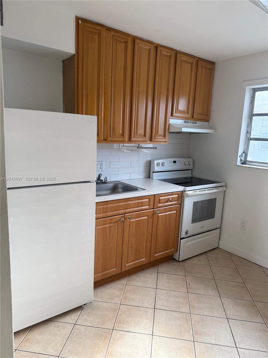 A small kitchen features wood cabinets, white appliances, a tiled backsplash, and light floor tiles — 767 SW 9th St # 202, Miami FL 33130, MIAMI, FL