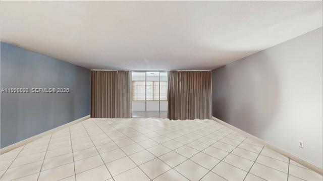 An empty room features light-colored tile flooring, blue and gray walls, and floor-to-ceiling curtains — 1401 NE 191st St # D117, Miami FL 33179, MIAMI, FL
