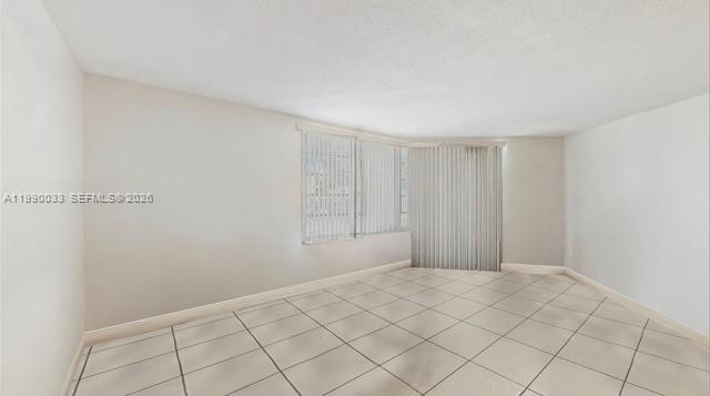 An empty room features white walls, light-colored tile flooring, and vertical blinds over the windows — 1401 NE 191st St # D117, Miami FL 33179, MIAMI, FL