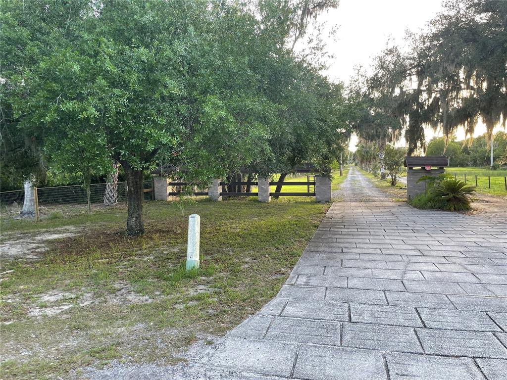A paved driveway leads toward a gated entrance surrounded by trees and a grassy yard — LAKE MARION ROAD W, HAINES CITY, FL