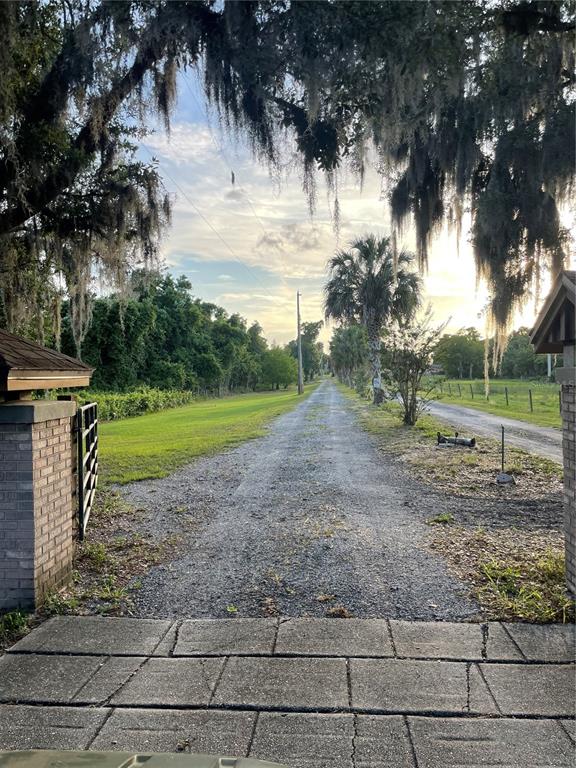 A gravel driveway leads through a gated entrance toward trees under a sunset sky — LAKE MARION ROAD W, HAINES CITY, FL