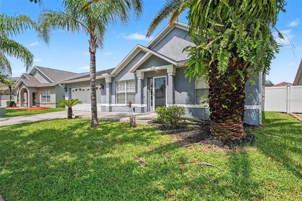 A single-story gray house with a palm tree in the front yard under a blue sky — 5146 NEW SAVANNAH CIRCLE, WESLEY CHAPEL, FL