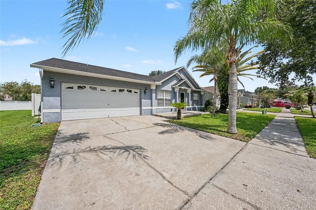 A single-story gray house with a two-car garage and a palm tree in the yard — 5146 NEW SAVANNAH CIRCLE, WESLEY CHAPEL, FL