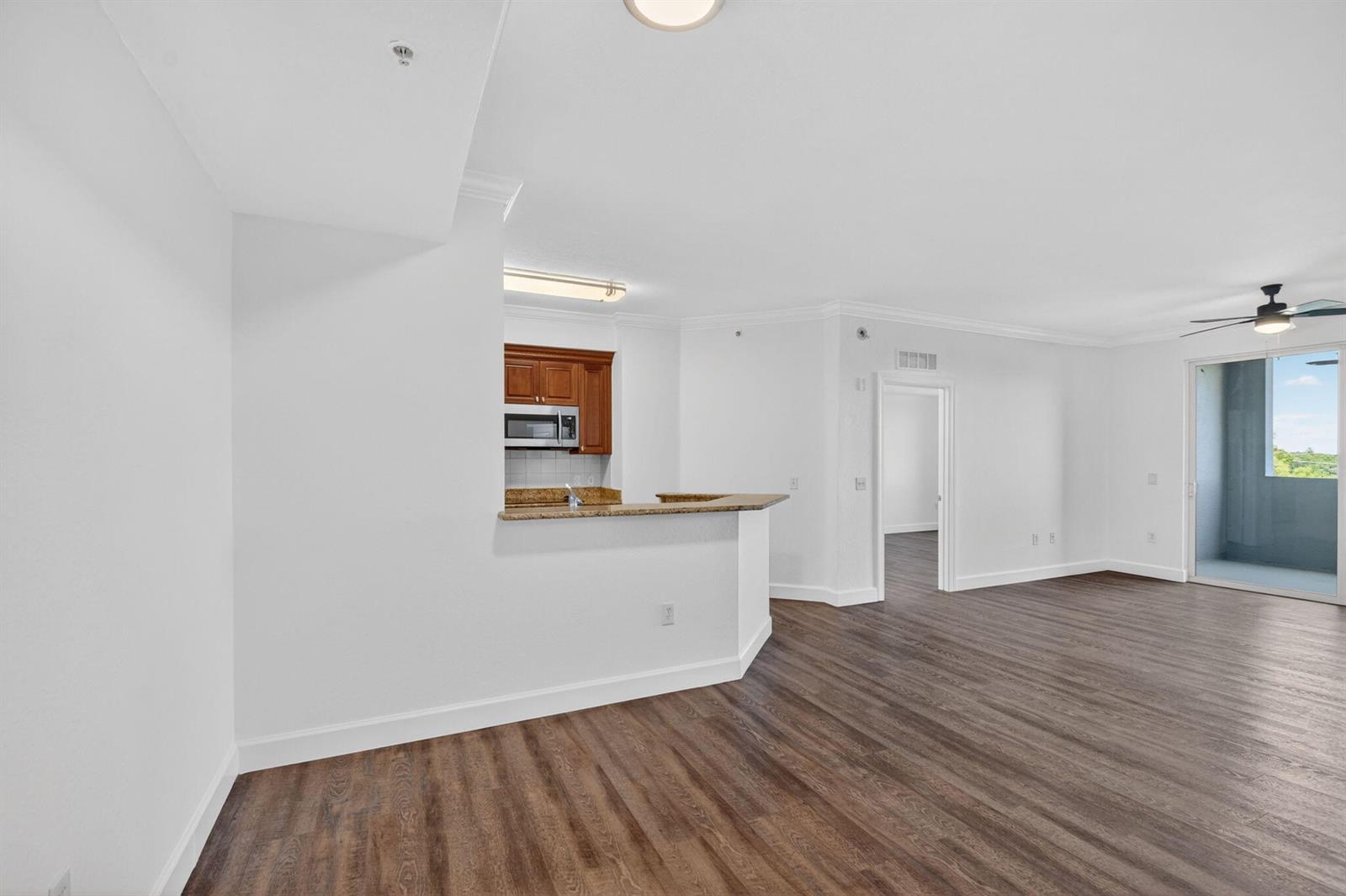 An open-concept living area features dark wood-look flooring, a kitchen with granite counters, and a balcony — 1660 Renaissance Commons Boulevard # 2407, Boynton Beach FL 33426, BOYNTON BEACH, FL