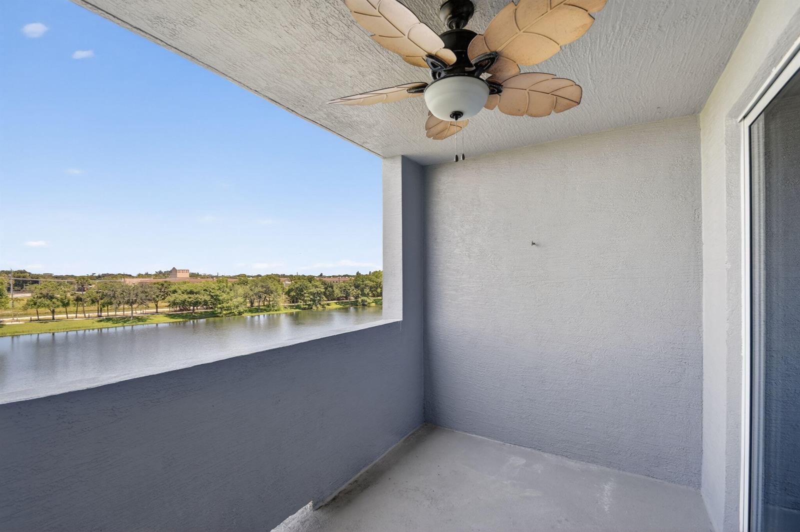 A balcony with a ceiling fan overlooks a lake and a treeline under a blue sky — 1660 Renaissance Commons Boulevard # 2407, Boynton Beach FL 33426, BOYNTON BEACH, FL