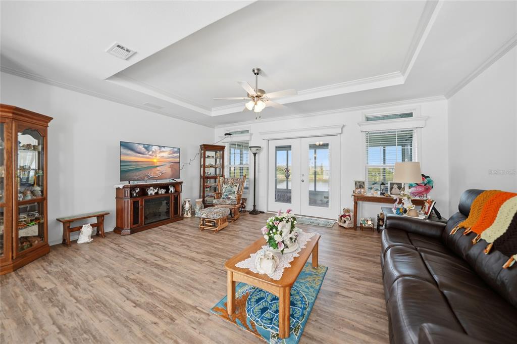 A living room features wood-look flooring, a tray ceiling, a television, and glass patio doors — 12116 SW COUNTY RD. 769 # 136, LAKE SUZY, FL