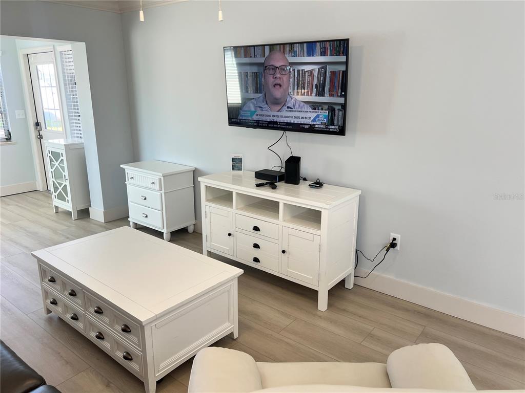 A living room features white furniture, light wood-look flooring, and a wall-mounted television — 6020 MIDNIGHT PASS ROAD UNIT 32, SARASOTA, FL