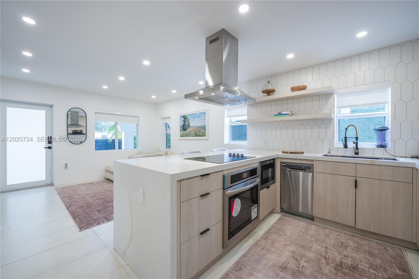 A modern kitchen features light wood cabinetry, white countertops, a central island, and tiled walls — 545 NW 47th St, Miami FL 33127, MIAMI, FL
