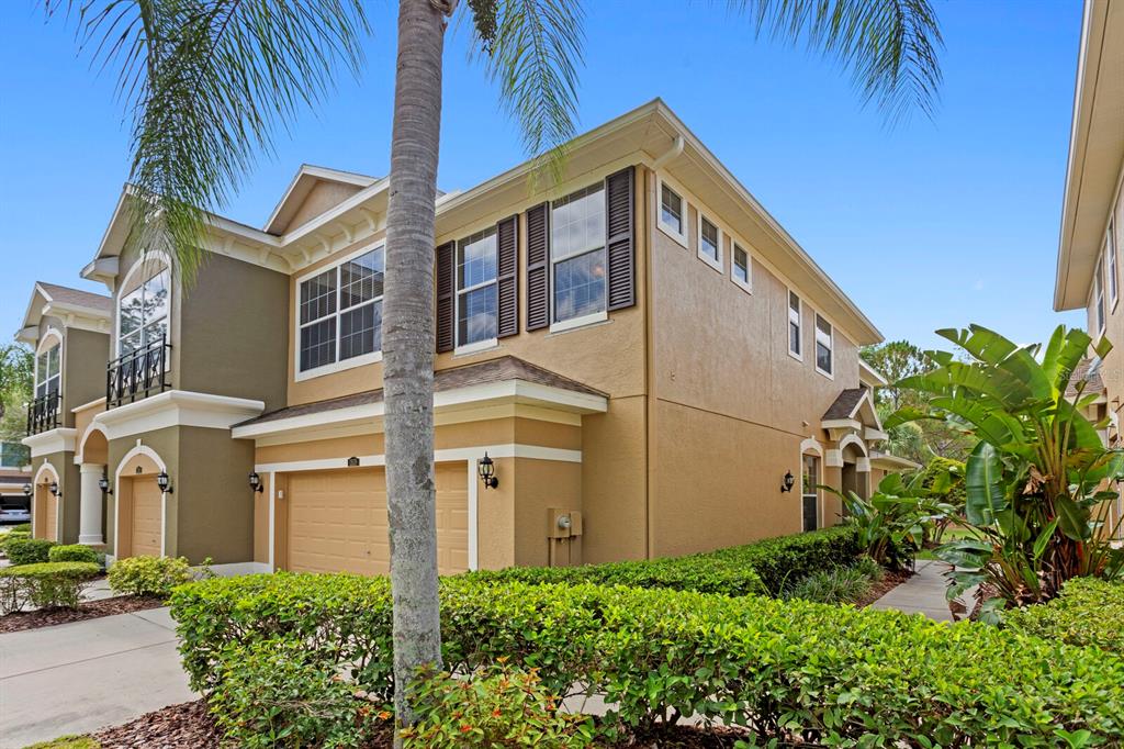 A two-story tan townhouse with a garage, dark shutters, and a manicured hedge in front — 12639 SILVERDALE STREET, TAMPA, FL