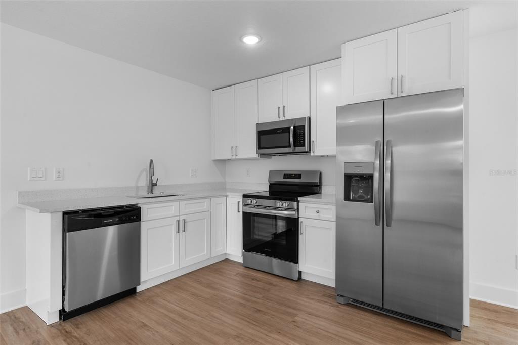 A kitchen featuring white cabinets, stainless steel appliances, and light wood-look flooring — 505 43RD STREET S UNIT 505 1/2, ST PETERSBURG, FL