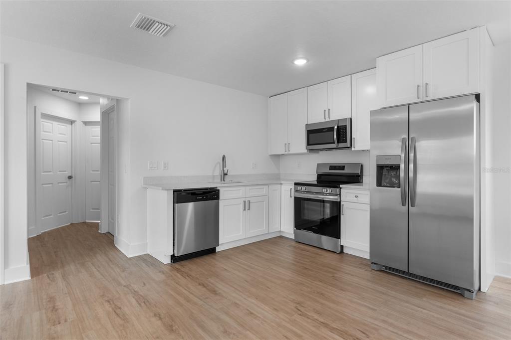 A modern kitchen features white cabinets, stainless steel appliances, and light wood-look flooring — 505 43RD STREET S UNIT 505 1/2, ST PETERSBURG, FL