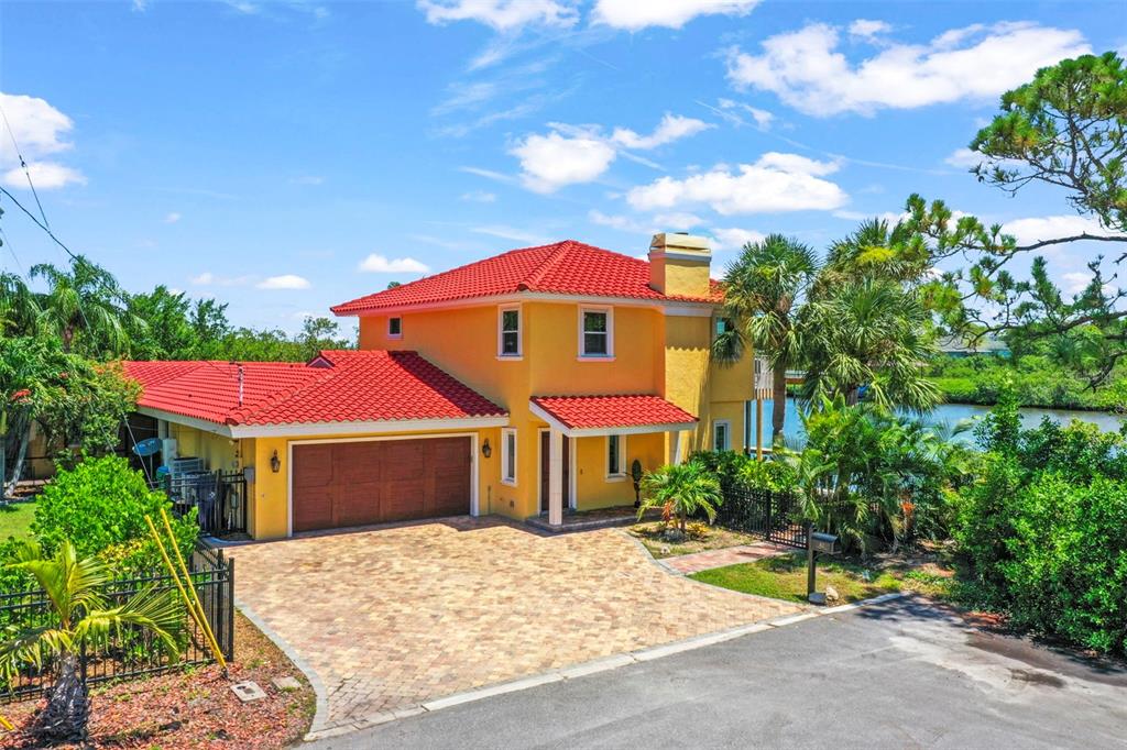 A two-story yellow house with a red tile roof and a brick-paved driveway — 412 ORCHID LANE, PALM HARBOR, FL