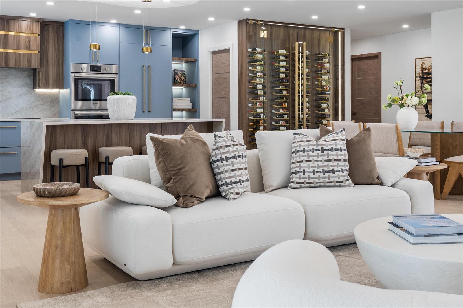 A modern open-concept living room features a white sofa, a kitchen with blue cabinets, and a wine wall — 2413 NW 26th Street, Boca Raton FL 33431, BOCA RATON, FL