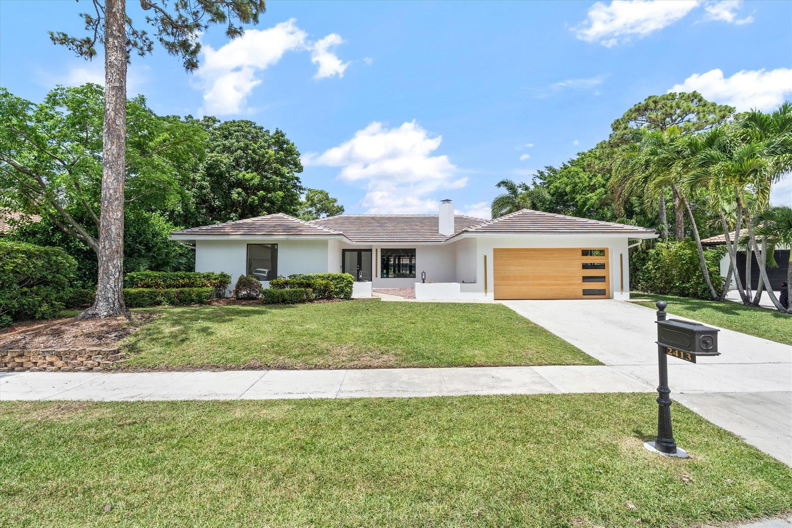 A single-story white house with a wooden garage door and a landscaped front yard — 2413 NW 26th Street, Boca Raton FL 33431, BOCA RATON, FL