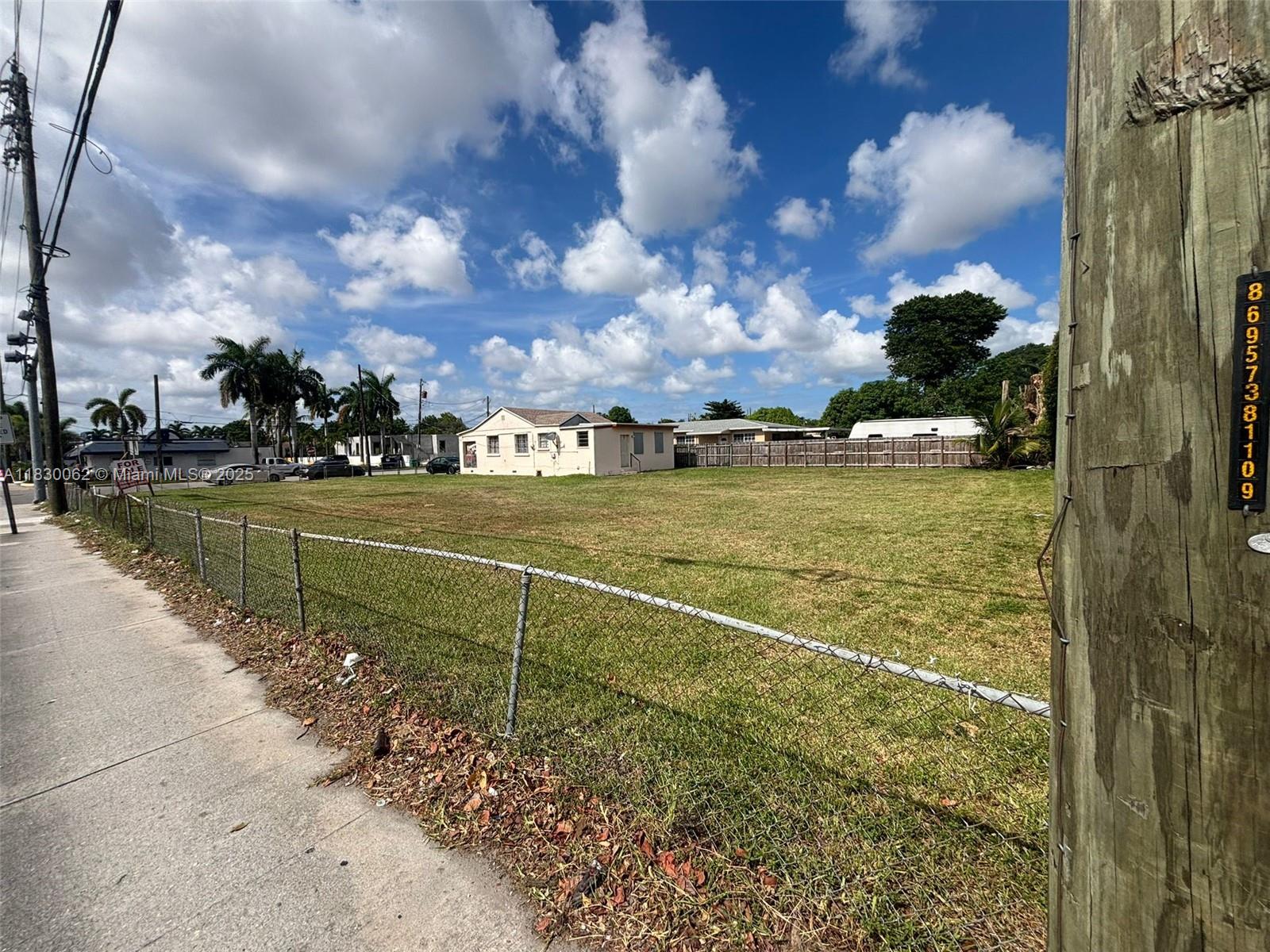 A vacant grassy lot is enclosed by a chain-link fence under a blue sky — 3186 NW 33rd St, Miami FL 33142, MIAMI, FL