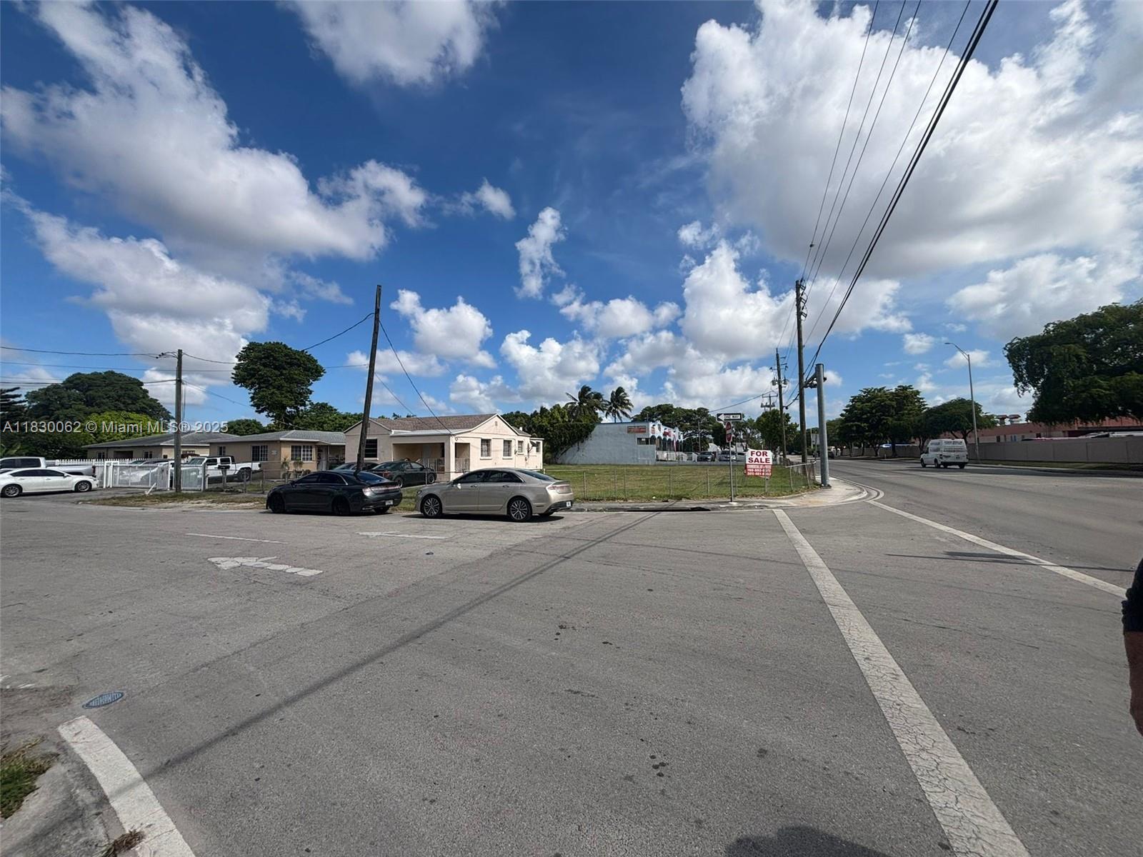 An exterior view shows a vacant corner lot with a for sale sign and parked cars — 3186 NW 33rd St, Miami FL 33142, MIAMI, FL