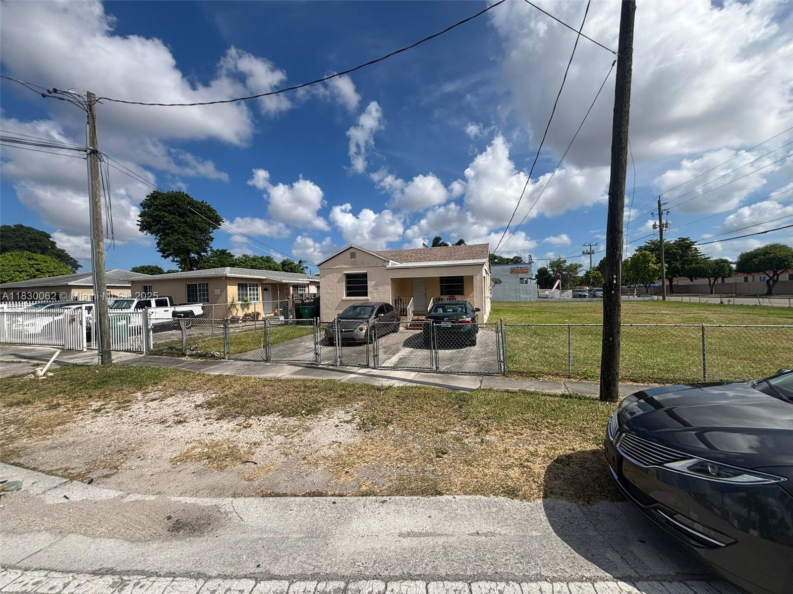 A single-story house with a paved driveway and chain-link fence sits under a cloudy sky — 3186 NW 33rd St, Miami FL 33142, MIAMI, FL