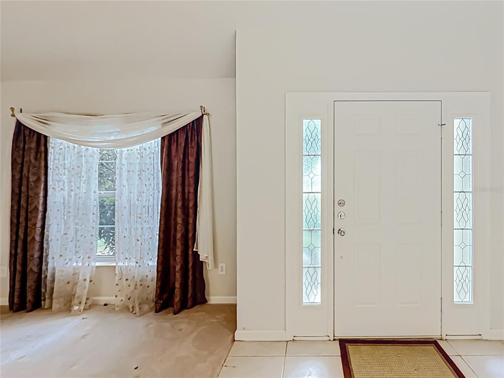 An entryway features a white front door with sidelights, a window with curtains, and tile flooring — 5669 SW 40TH STREET, OCALA, FL