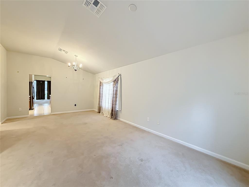 An empty living room features beige carpeting, white walls, a vaulted ceiling, and a chandelier — 5669 SW 40TH STREET, OCALA, FL