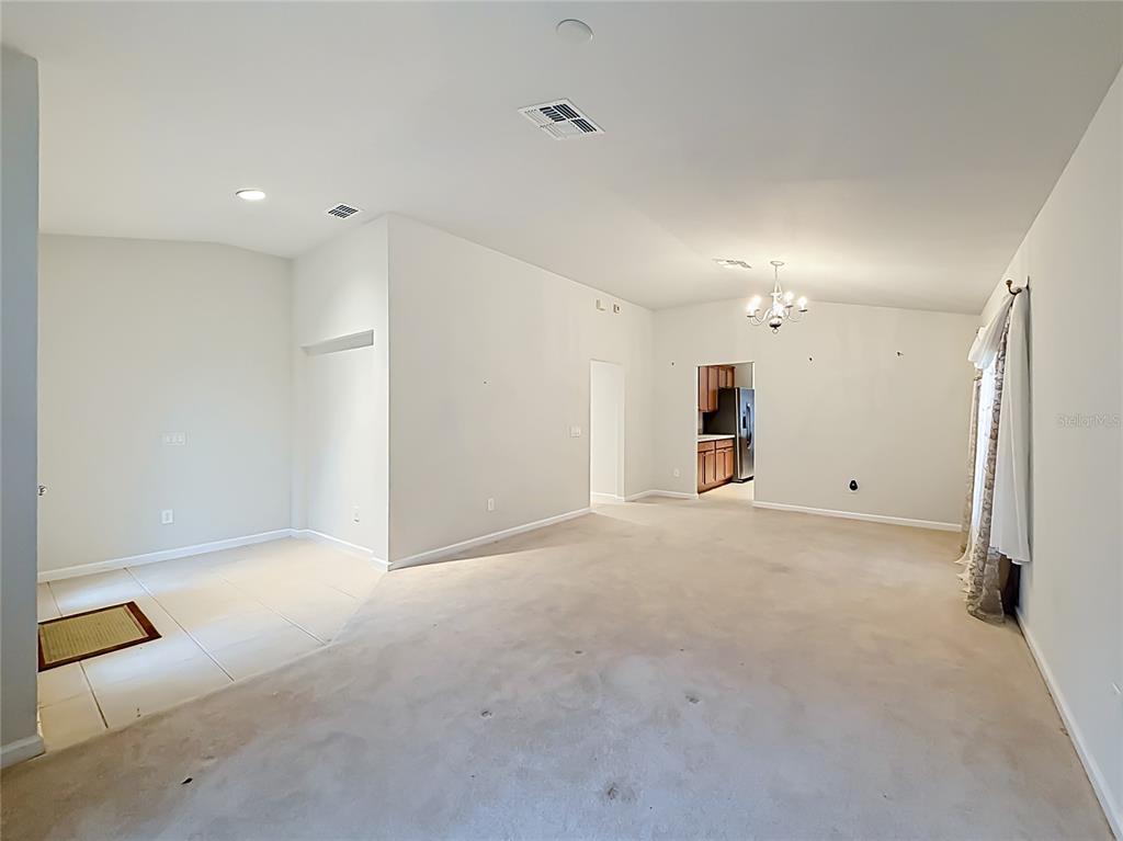 An open-concept living area features beige carpeting, tiled flooring near the entrance, and a chandelier — 5669 SW 40TH STREET, OCALA, FL