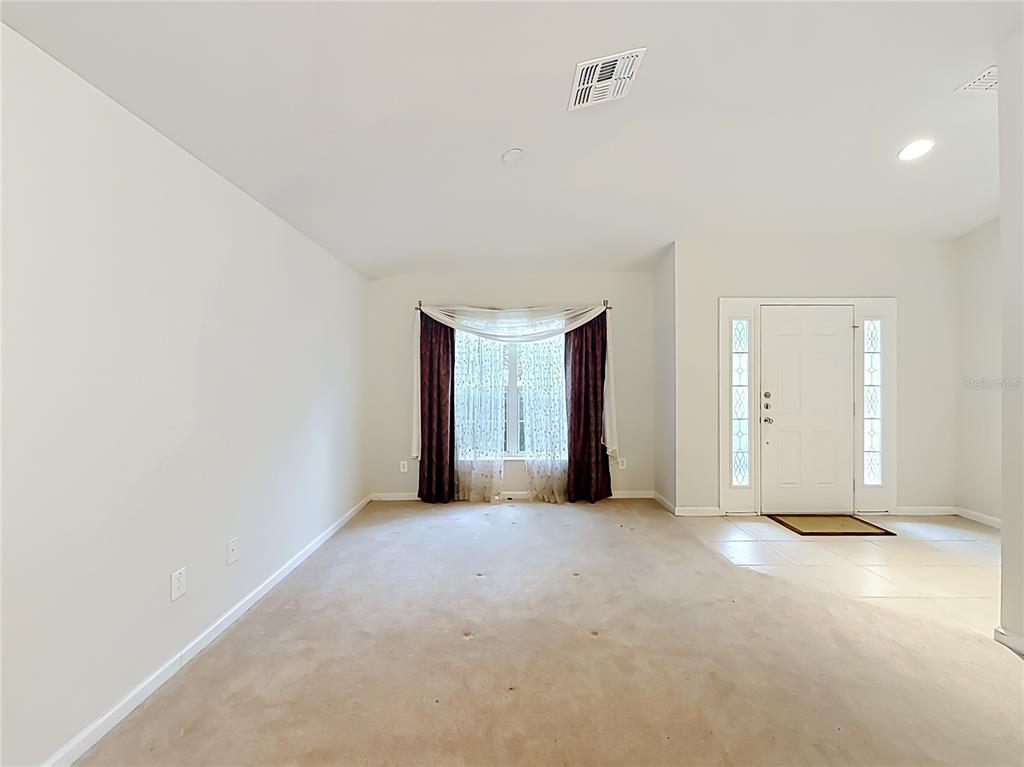 A carpeted living room features a front door with sidelights and a window with curtains — 5669 SW 40TH STREET, OCALA, FL