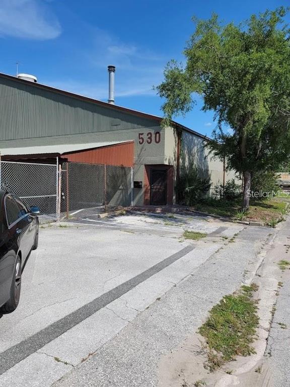 A low-angle exterior view of a warehouse building with a metal roof and fenced entrance — 530 NW 1ST AVENUE, OCALA, FL