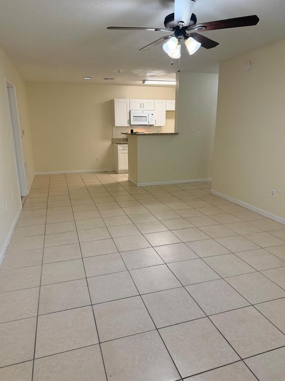 An open-concept living area features light-colored floor tiles, a ceiling fan, and a kitchen beyond — 4308 S KIRKMAN ROAD UNIT 1713, ORLANDO, FL