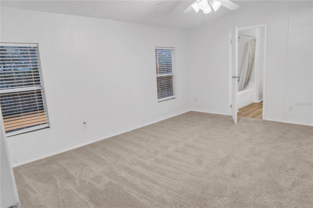 A bedroom with white walls, beige carpet, two windows with blinds, and an attached bathroom — 7311 20 TH STREET, ZEPHYRHILLS, FL