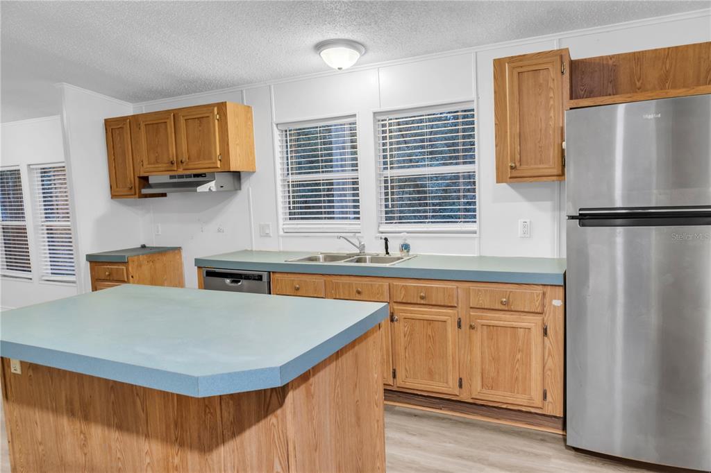 A kitchen features wooden cabinets, a light blue countertop, a stainless steel refrigerator, and an island — 7311 20 TH STREET, ZEPHYRHILLS, FL