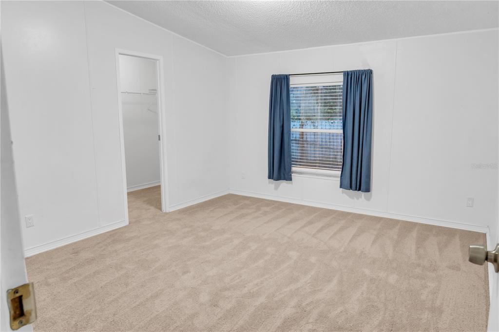 A bedroom with white walls, beige carpeting, a window with blue curtains, and a closet — 7311 20 TH STREET, ZEPHYRHILLS, FL