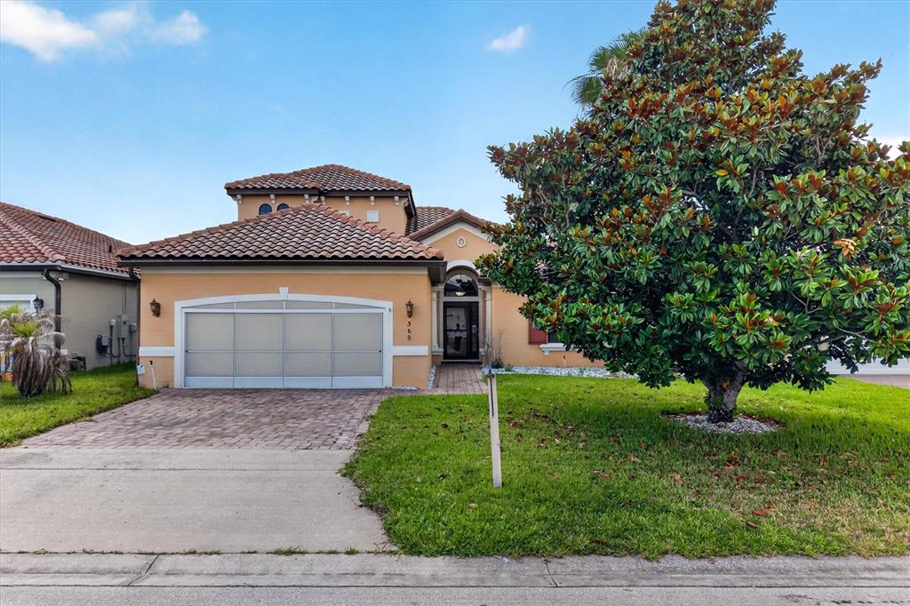A single-story house with a tan stucco exterior, a tiled roof, and a large tree — 369 VILLA SORRENTO CIRCLE, HAINES CITY, FL