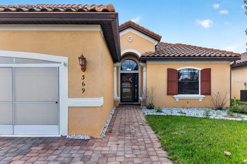 A tan stucco house exterior features a tiled roof, arched entryway, and a brick walkway — 369 VILLA SORRENTO CIRCLE, HAINES CITY, FL