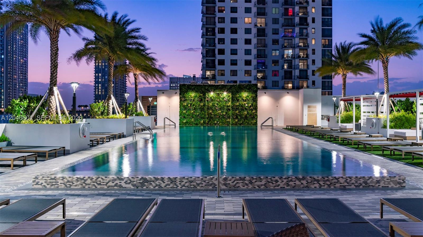 A swimming pool with a green wall feature is surrounded by lounge chairs at dusk — 650 NE 2nd Ave # 1811, Miami FL 33132, MIAMI, FL