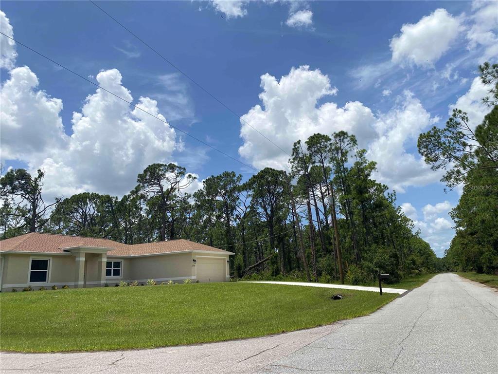 A single-story house with a tan exterior and a two-car garage sits beside a road — KAMSLER AVE, NORTH PORT, FL