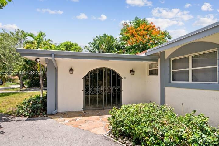 A white house exterior features a covered entryway with a decorative metal gate — 13325 SW 84th Ave, Pinecrest FL 33156, PINECREST, FL