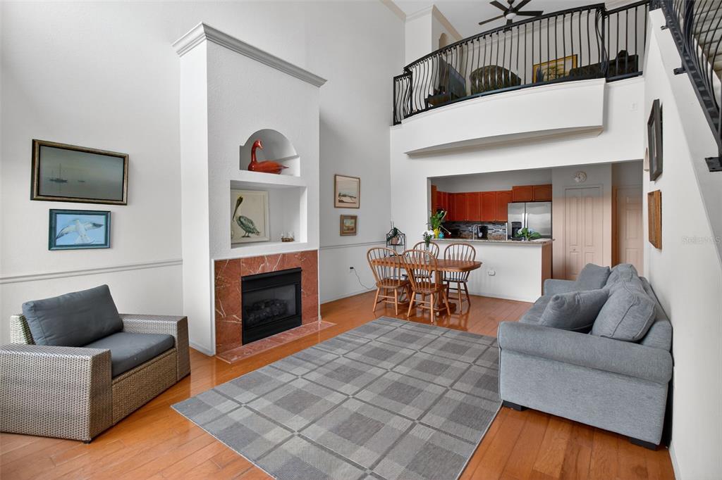 A living room with a fireplace, hardwood floors, and an open view to the kitchen — 2746 VIA TIVOLI UNIT 116A, CLEARWATER, FL