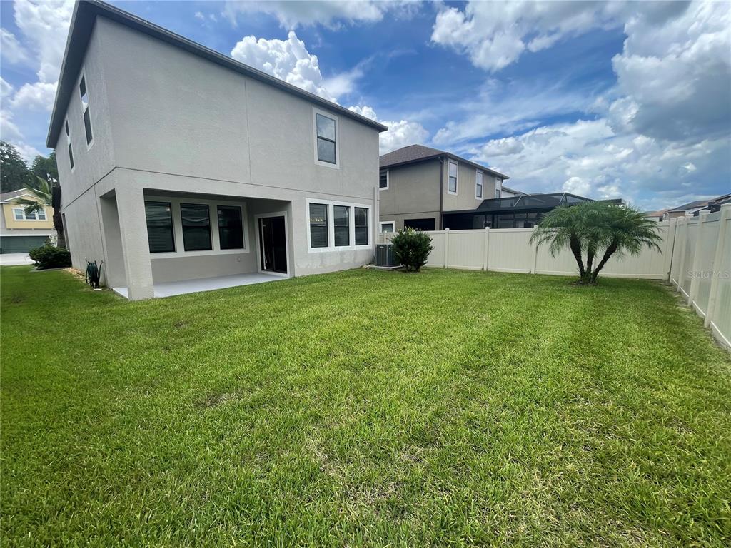 The backyard of a two-story house features a concrete patio, lawn, and vinyl fencing — 1596 LUDINGTON AVENUE, WESLEY CHAPEL, FL