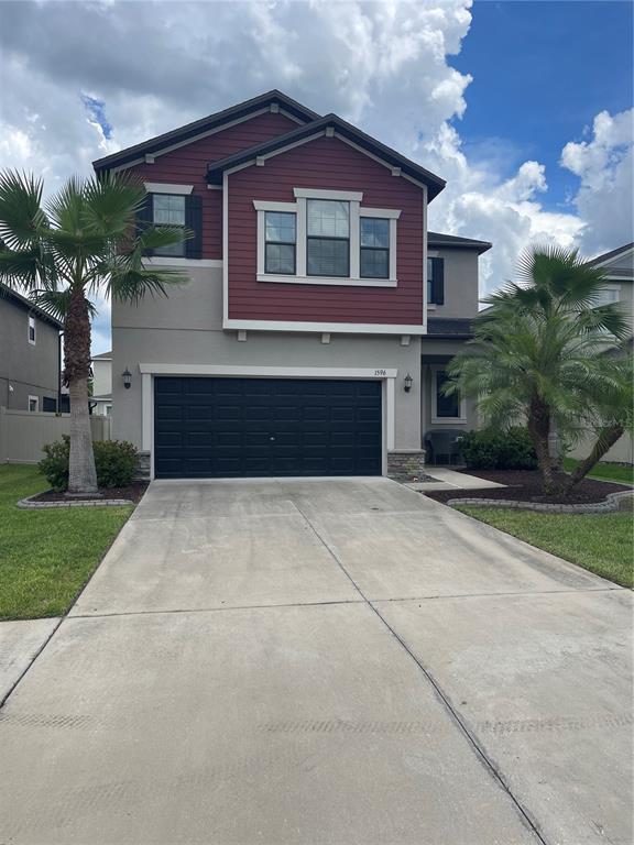 A two-story house with a red-accented upper level, a black garage door, and palm trees — 1596 LUDINGTON AVENUE, WESLEY CHAPEL, FL